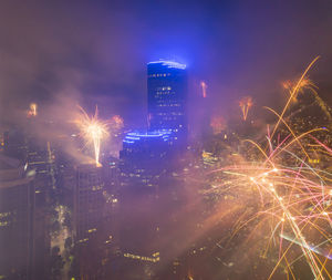 Firework display in city against sky at night