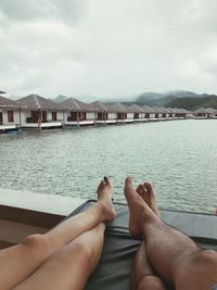 Low section of people relaxing on water against sky