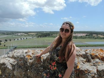 Young woman wearing sunglasses standing by rock against agricultural field