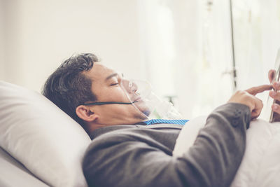 Side view of patient using smart phone while lying on bed in hospital