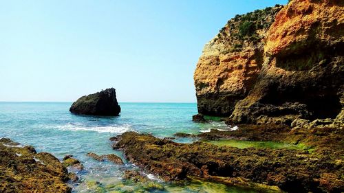 Rock formations by sea against clear sky