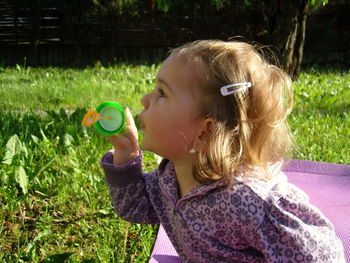 Close-up of cute girl blowing bubbles while sitting at park