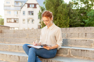 Woman holding book while sitting on steps