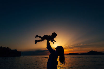 Silhouette people on beach against sky during sunset