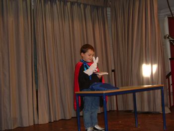 Full length of smiling boy wearing cape performing on stage against curtain