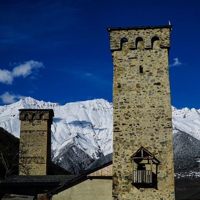 architecture, built structure, building exterior, snow, winter, cold temperature, low angle view, sky, blue, religion, mountain, tower, sunlight, church, day, cloud - sky, no people, white color, stone wall