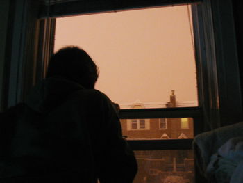 Rear view of people looking through window at home