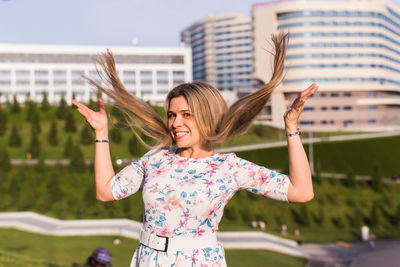 Happy woman with arms raised standing against built structure