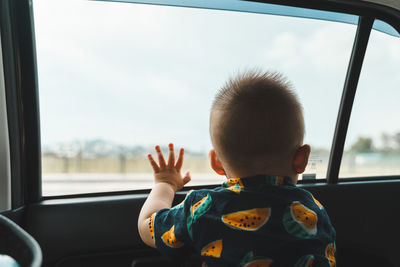 Rear view of boy looking through window