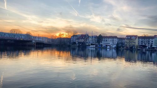 Sailboats in river by buildings against sky during sunset