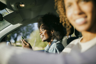 Smiling young woman with smart phone sitting by friend in car