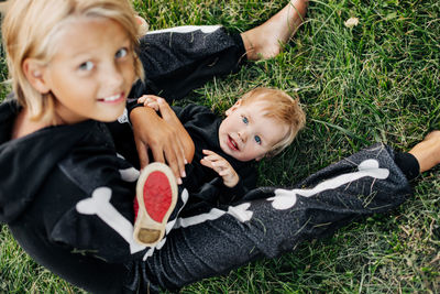 A girl in a hat and a skeleton costume plays with her younger brother on the grass in the garden. 