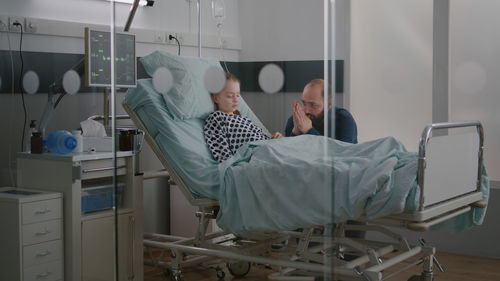 Man praying for daughter while sitting by hospital bed