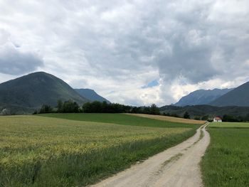 Empty road amidst field against sky