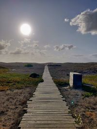 Boardwalk leading towards landscape against sky