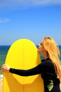 Woman standing with yellow surfboard against sky