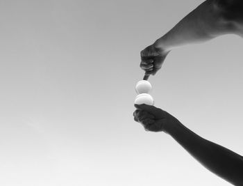 Low angle view of person balancing crystal balls against clear sky