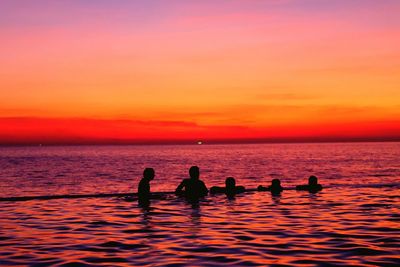 Silhouette people on sea against orange sky