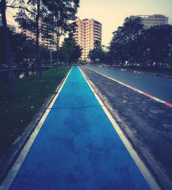 Empty road by buildings in city against sky