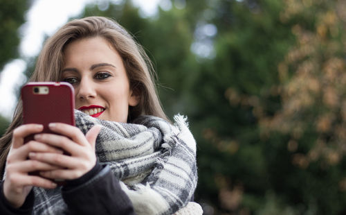 Smiling young woman using smart phone during winter