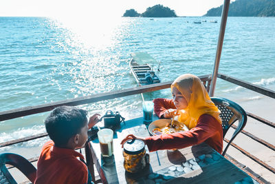 High angle view of boy and girl eating food on table against sea