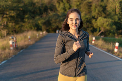 Happy attractive young woman wearing her warm up jacket while running at a local park