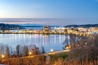 Illuminated buildings by lake against sky in city at night