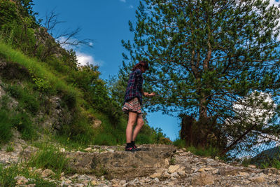 Low angle view of person standing by trees against blue sky