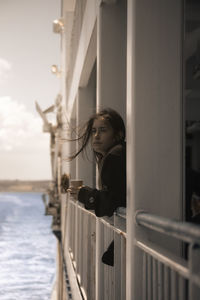 Side view of woman looking at railing against sky