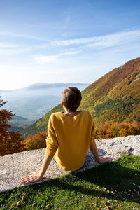 Young woman is sitting and looking at autumn landscape in italy. 