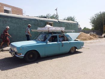 Side view of young woman on car against sky