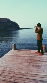 Man photographing at sea shore against clear sky