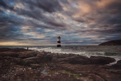 Lighthouse by sea against sky during sunset