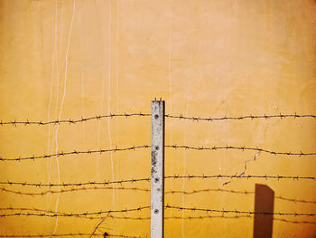 Post and barbed wires with shadows against old yellow wall