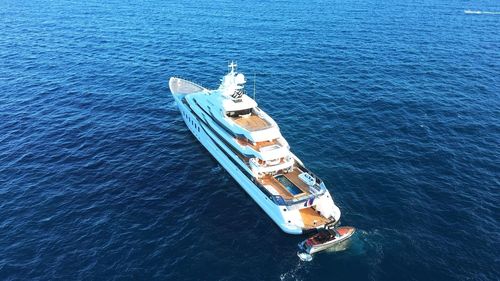 Superyacht with pool and helicopter landing space, in the water with its tender