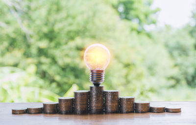 Close-up of light bulb on stacked coins at table in yard