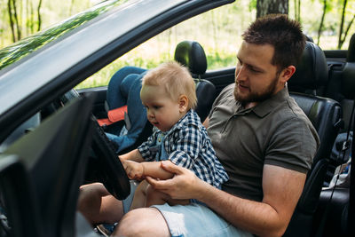 Dad shows his little son how to drive car while sitting behind wheel