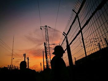 Silhouette men by electricity pylon against sky during sunset