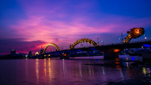 A bridge spanning the river under the colorful colors of the sunset sky. 