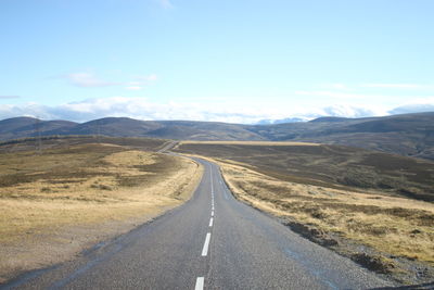 Empty road leading towards mountain against sky