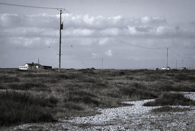 Electricity pylon on field against cloudy sky