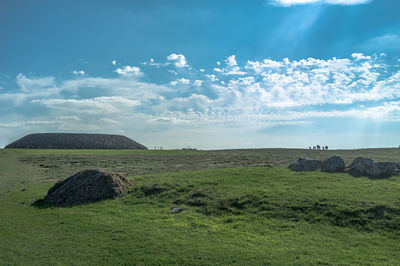 Scenic view of green landscape against cloudy sky on sunny day