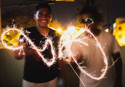 Portrait of happy man with friends holding sparklers at night