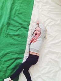 High angle view of cheerful girl lying on bed at home
