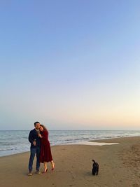 Rear view of woman and man standing at beach against clear sky