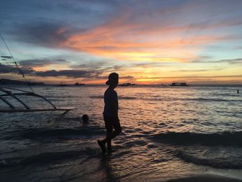 Silhouette man standing on beach against sky during sunset