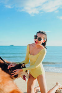 Portrait of woman wearing sunglasses while standing at beach against sky