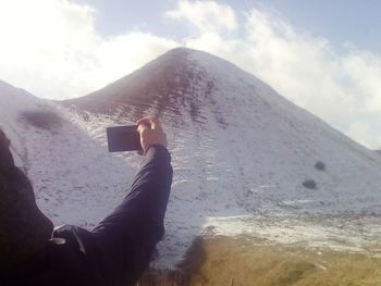Man photographing on snow covered mountain against sky