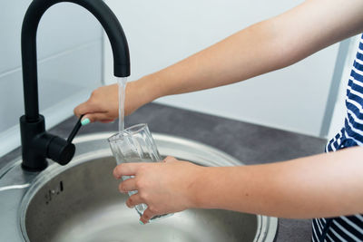Midsection of woman filling water in glass from faucet