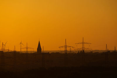 Silhouette electricity pylons against orange sky